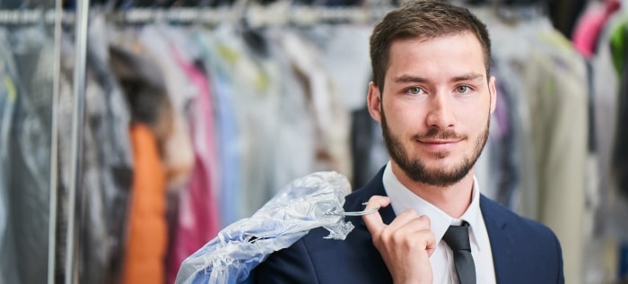 man smiles while holding dry cleaning