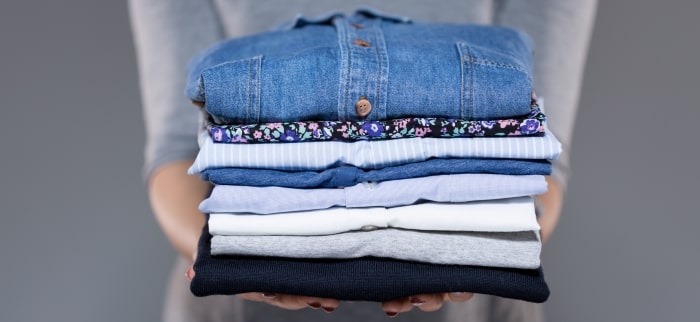 Woman Holding Stack Of Folded Laundry Min